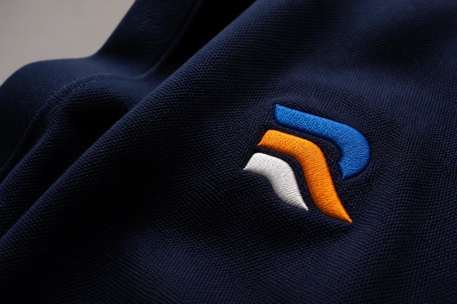 Close-up of raised blue, orange, and white embroidery stitches on navy fabric